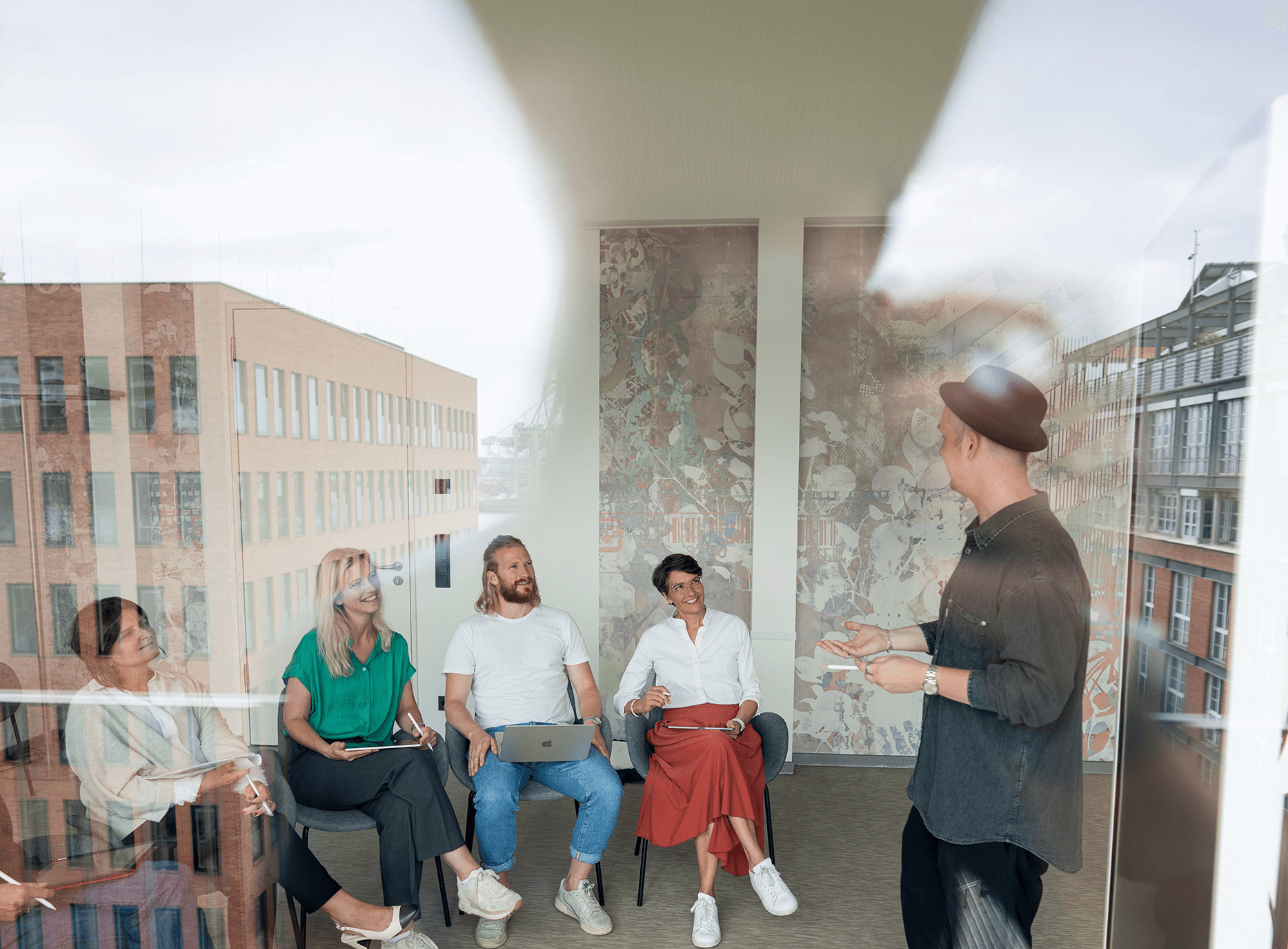 Organisationsentwickler:in-Ausbildung – Trainer spricht mit Gruppe im Seminarraum, Blick durch Glasfront mit Spiegelung“