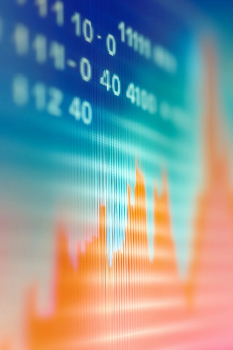 Abstrakte Nahaufnahme eines Computerbildschirms, der eine unscharfe, leuchtende Grafik mit einem Finanz- oder Business-Intelligence-Chart in Orange- und Blautönen zeigt.