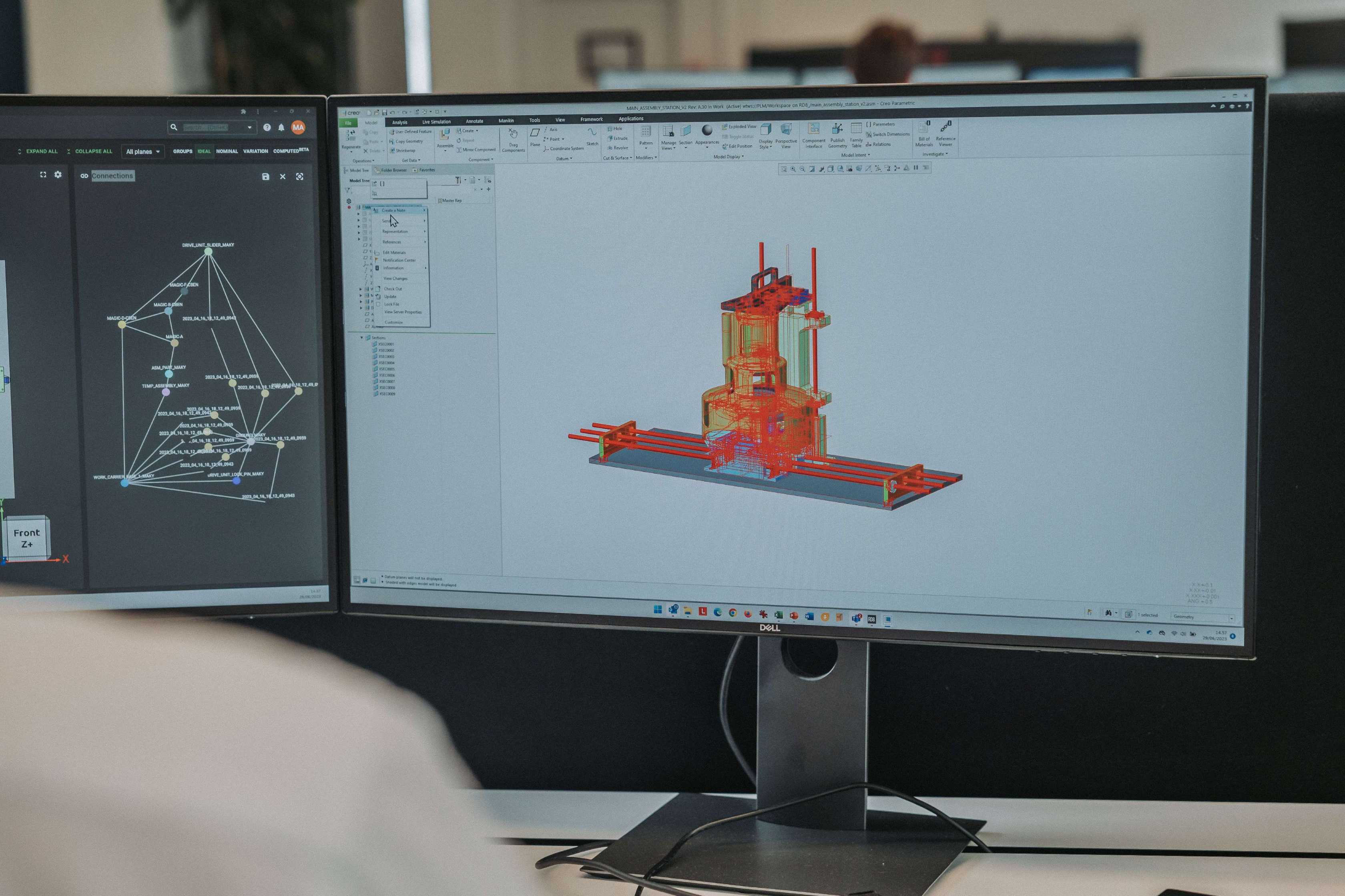 Dual computer monitors showing 3D CAD modeling software with an engineering design and a connection diagram.