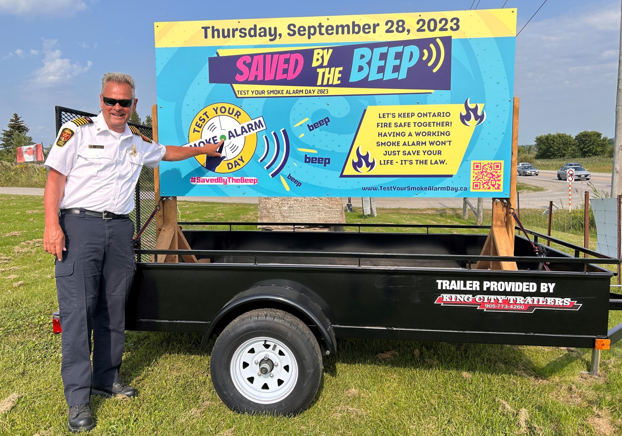 Fire service member in front of a large "Saved by the Beep!" campaign poster.