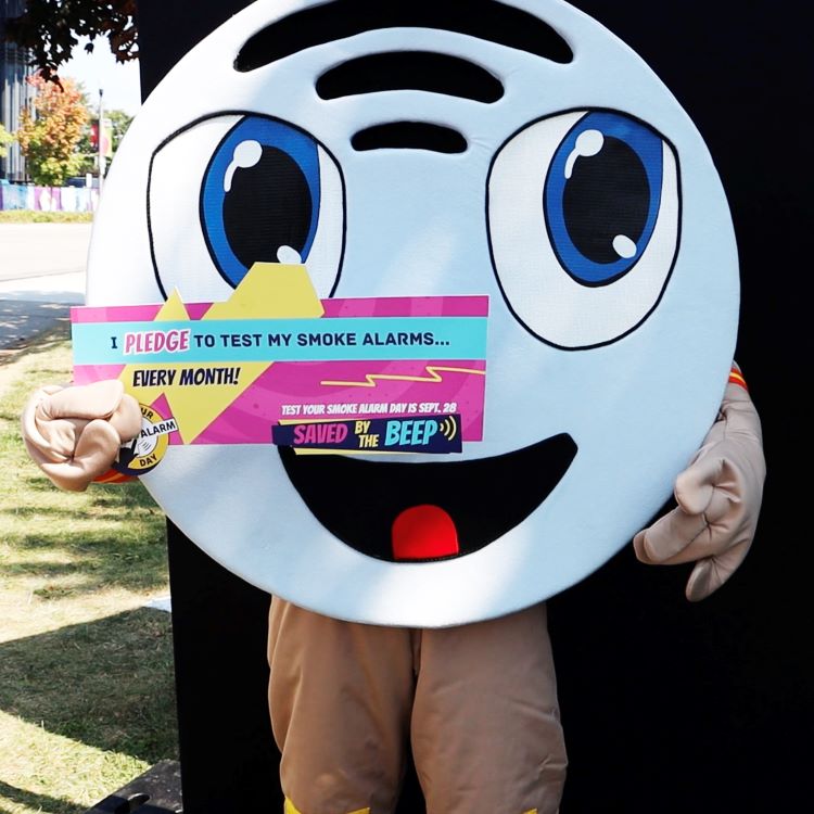 Smoke alarm mascot, Beepa, holding a sign pledging to test their smoke alarms