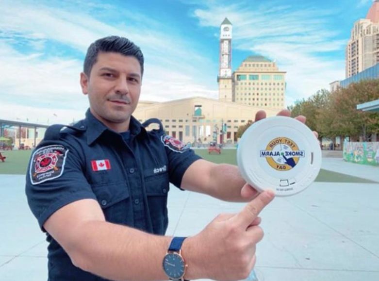 image of a fire service member showing a smoke alarm with a Test Your Smoke Alarm Day logo on it.