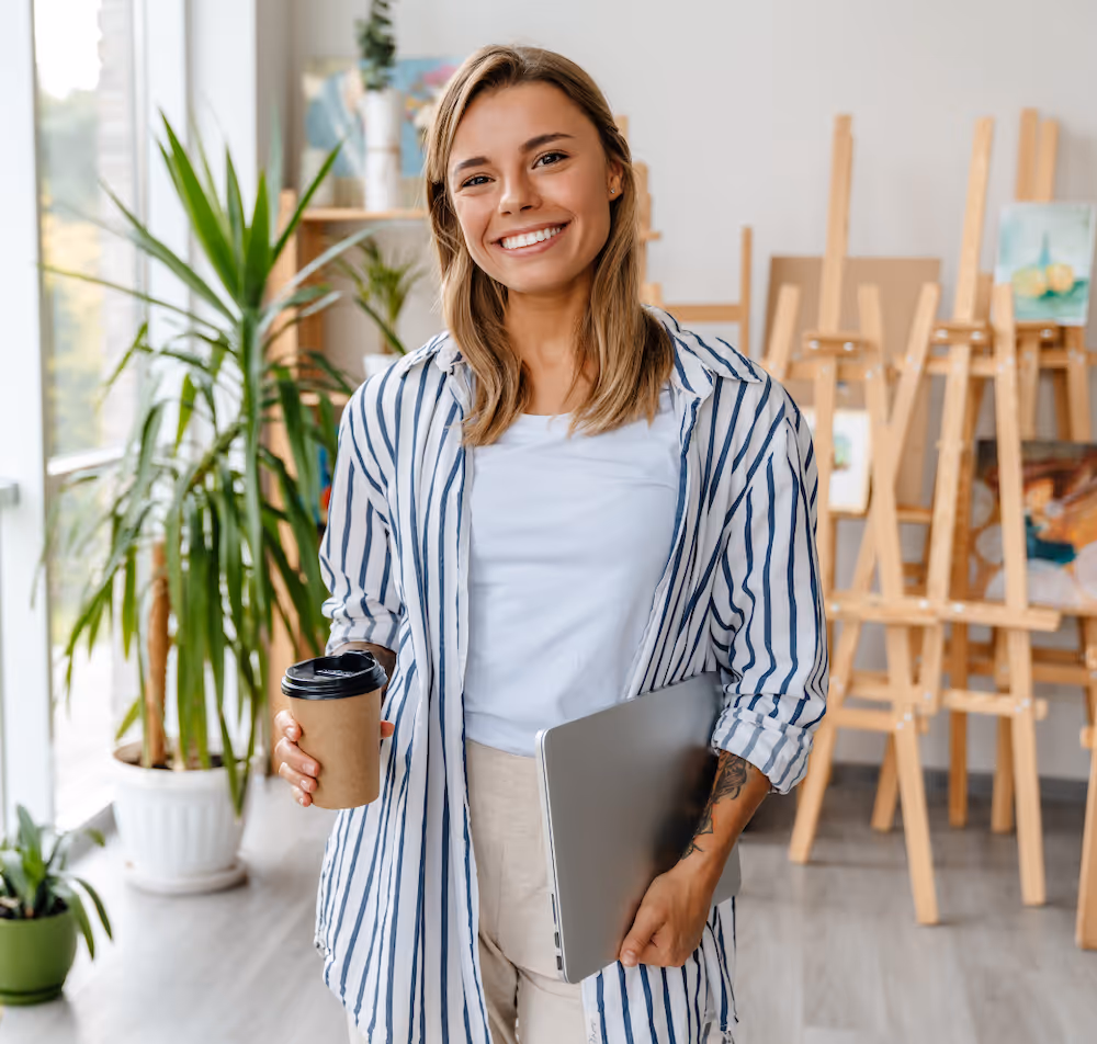 A woman holding a cup of coffee and a laptop.