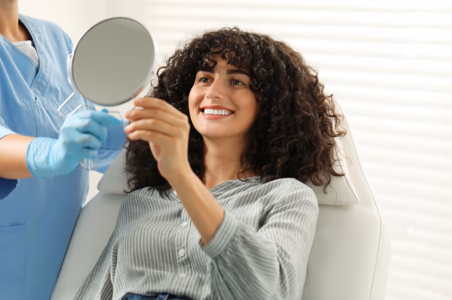 A woman sitting in a dentists chair holding a mirror.