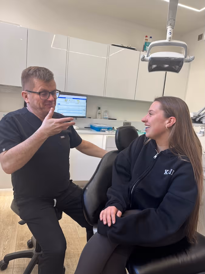 Dentist in black scrubs talking and smiling with a female patient seated in a dental chair in a modern dental office.