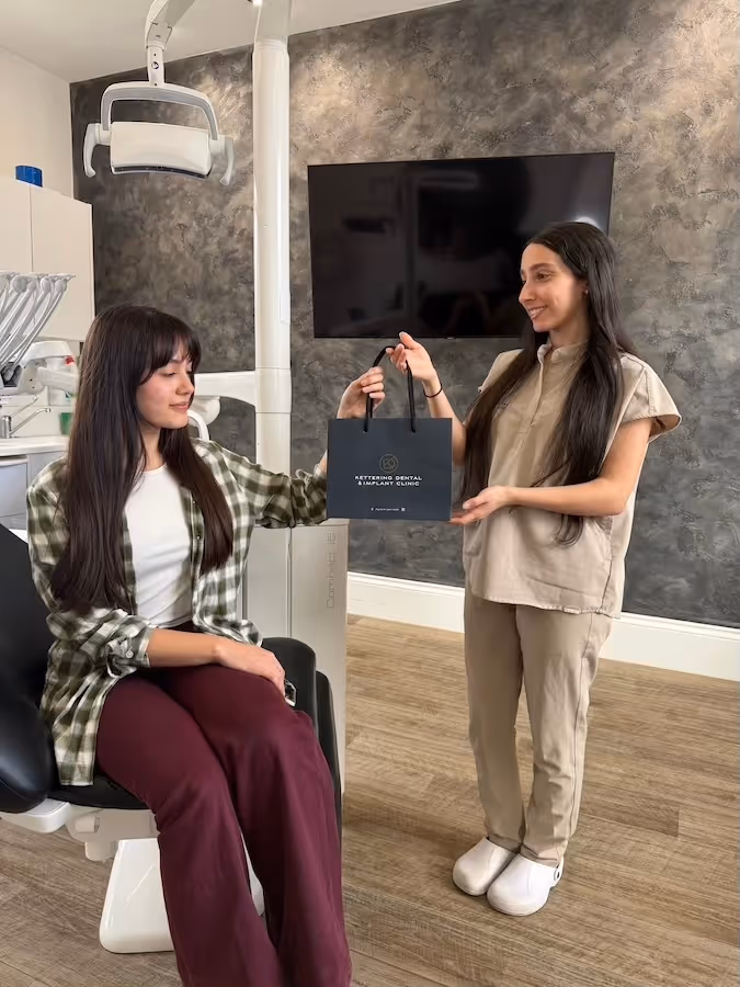 Dental clinic staff member handing a black gift bag to a seated patient in the dental office.