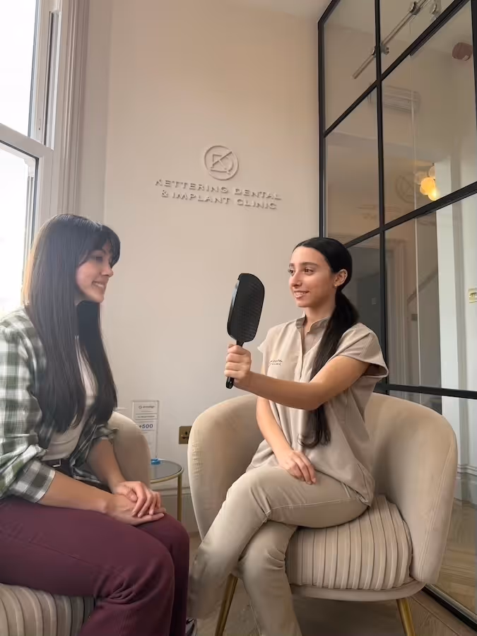 A dental professional holding a hand mirror for a female patient to view her teeth in a dental clinic waiting area.