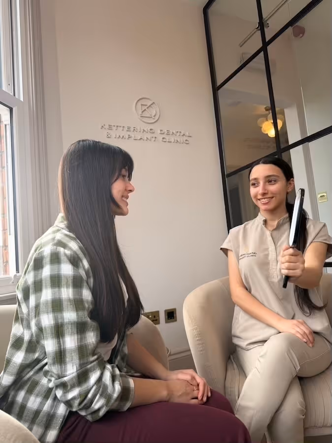 Dental professional in beige uniform holding a mirror showing a smiling patient her teeth at Kettering Dental & Implant Clinic.