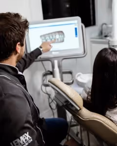 dentist explaining a patient about her dental malocclusion, he is pointing at the screen showing her teeth
