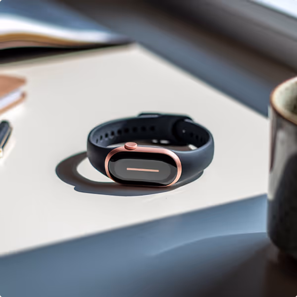 Closeup of the Kinētiq wellness tracker resting on a table in natural sunlight, highlighting its sleek design and minimalist form.