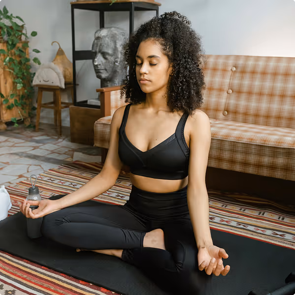 Woman meditating peacefully in her living room, symbolizing hormonal cycle awareness and stress management with Kinētiq wellness tracker.