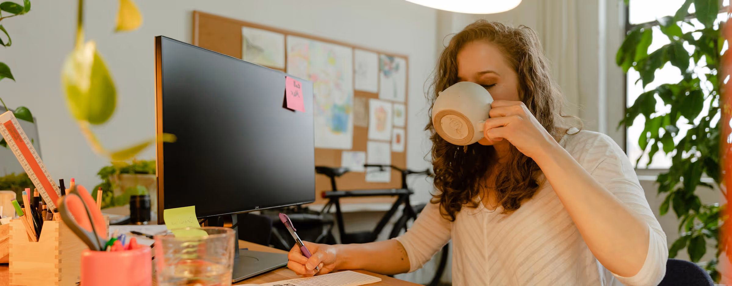 Woman working at a desk drinking coffee in the afternoon, representing focus and energy management with Kinētiq’s health monitoring device.