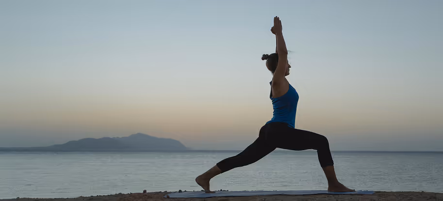A woman doing yoga by the lakeside with a small mountain in the background.