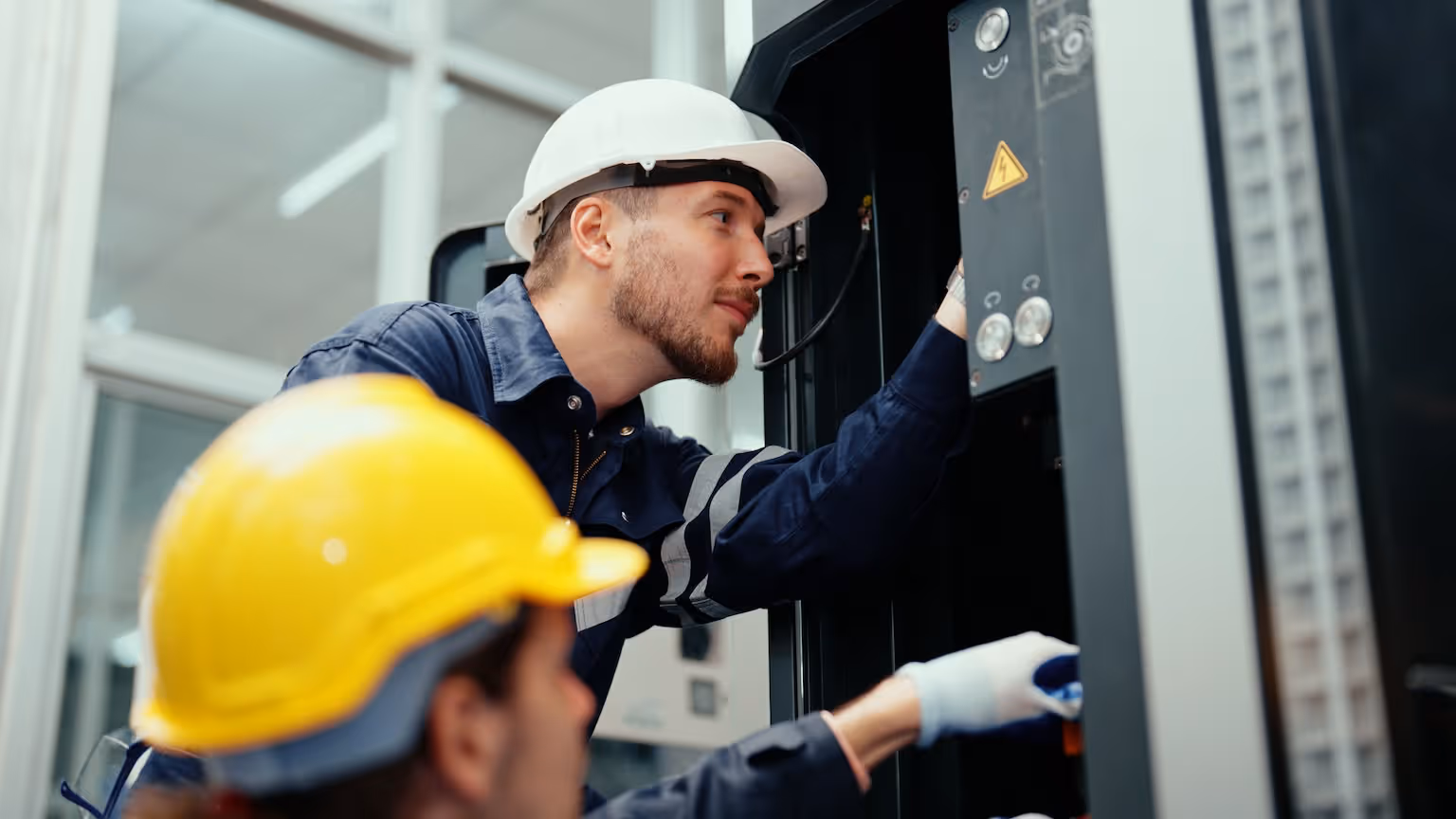 Two electricians inspecting an industrial breaker panel.