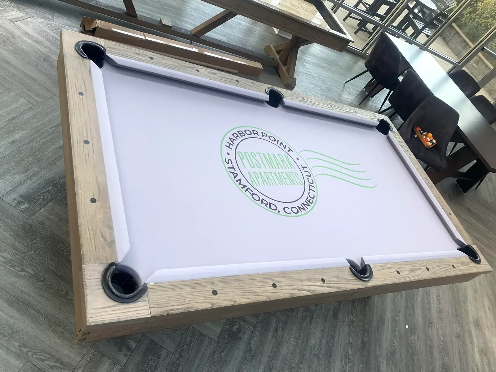 A large, rectangular pool table with a grey felt top and the "Harbor Point" logo in green. The table has a wooden frame and is in a well-lit room with tables and chairs in the background.