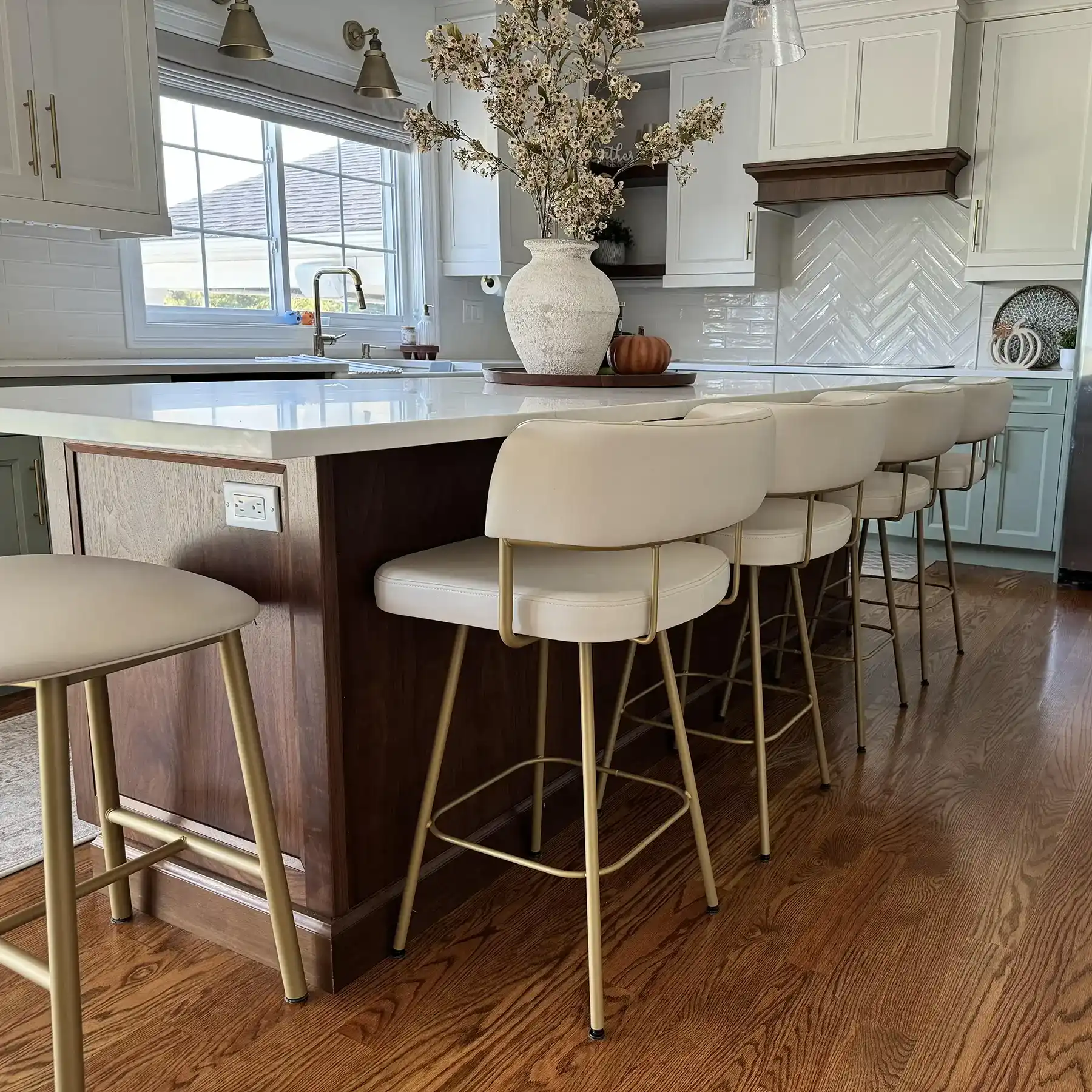 Kitchen island with five white bar stools and a vase of flowers.