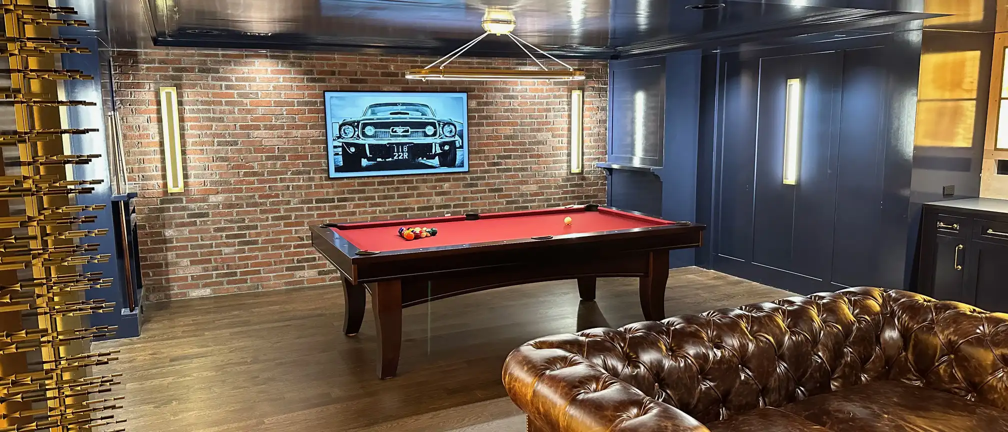 Richly decorated game room with a Brunswick Winfield Espresso pool table ready for a game, complemented by a tufted leather sofa and a wine display.