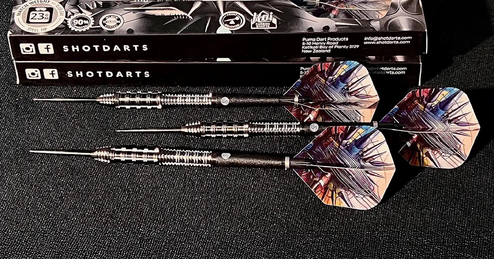Three Shot Darts Puma steel tip darts arranged with sleek black and orange packaging. High-quality 90% tungsten barrels for enhanced performance. Shot Darts brand prominent. Perfect for competitive players.