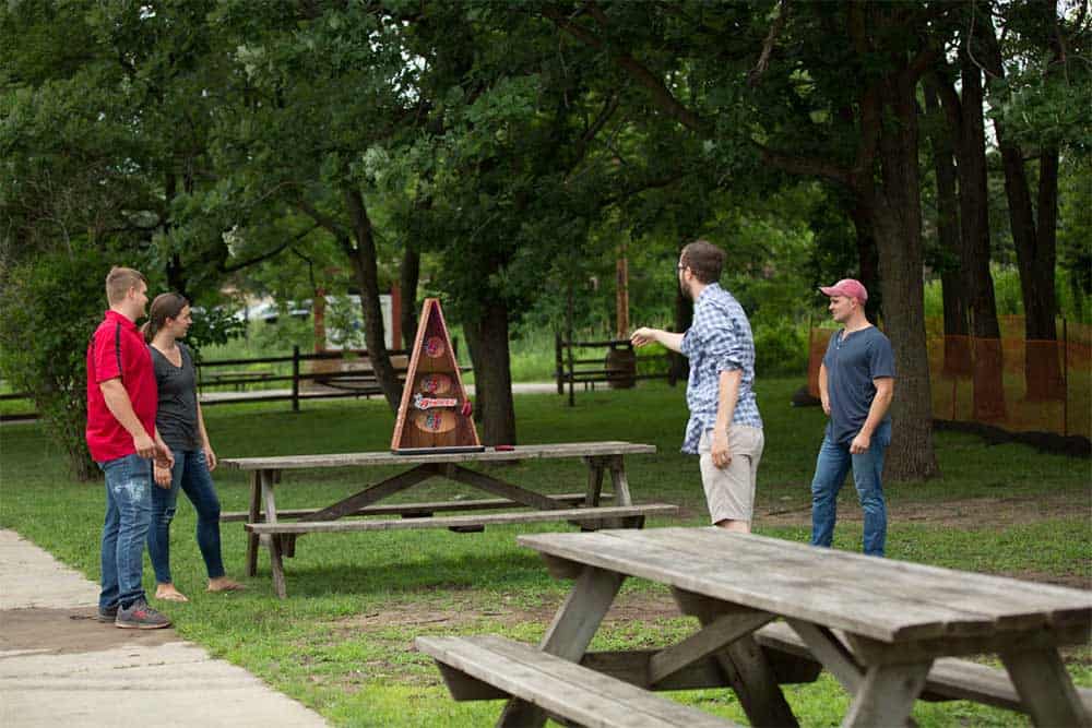people playing bosstoss or aholes outside in a park with a picnic table