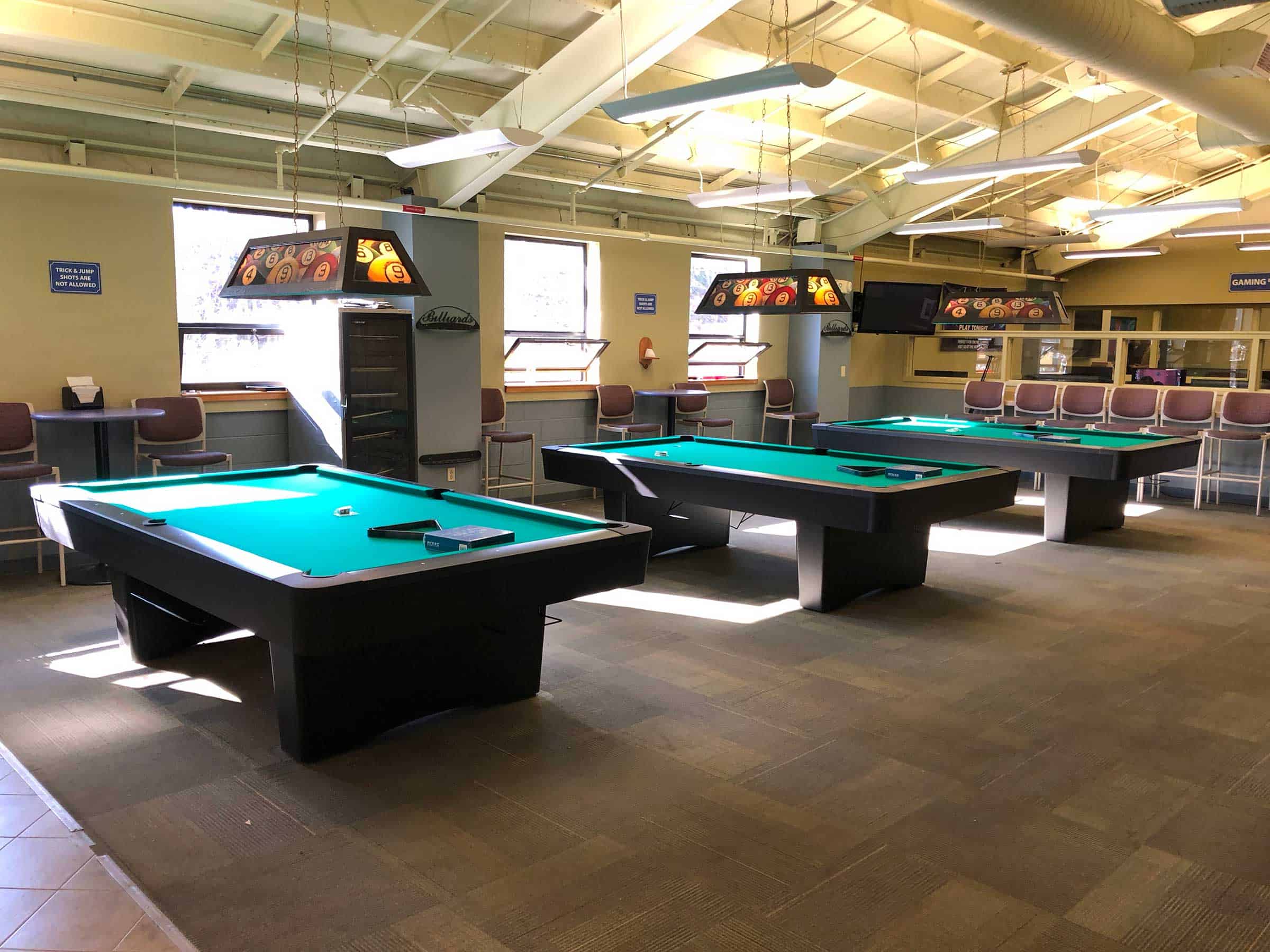 three green felt pool tables with billiard lighting