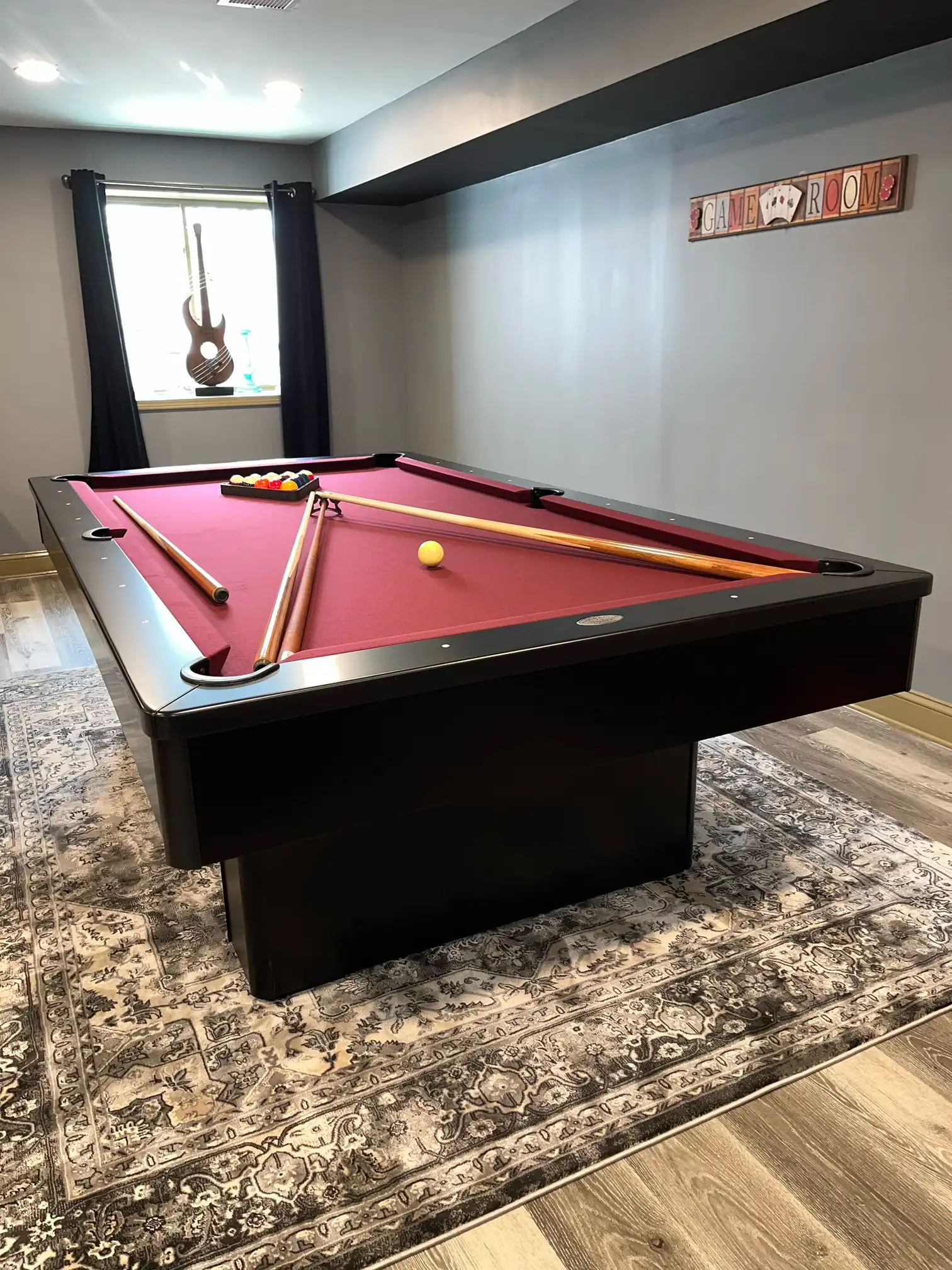 red olhausen monarch pool table with a guitar in the background and a game room sign on the wall on a nice rug