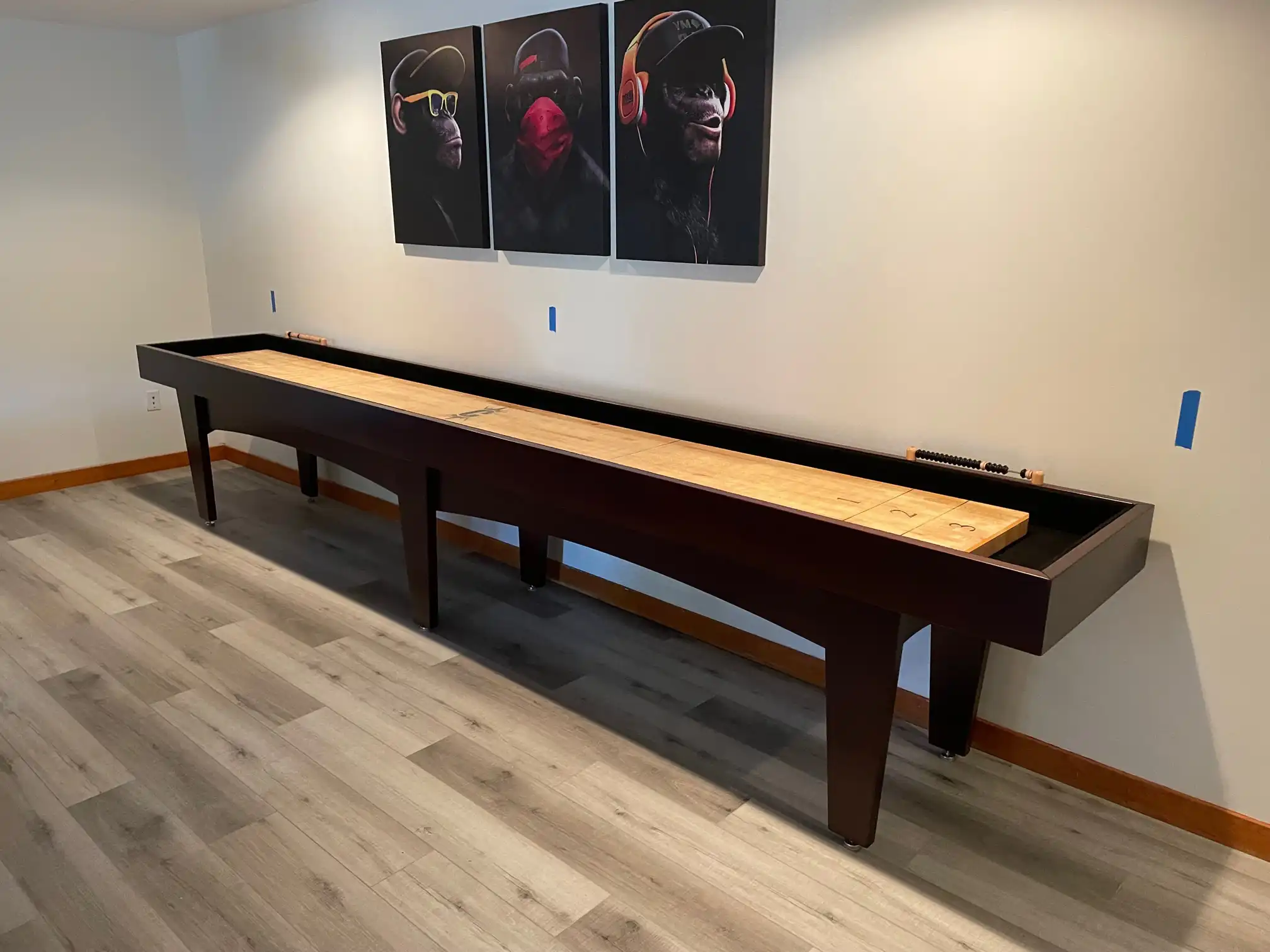 shuffleboard table against a wall with 3 posters of monkeys