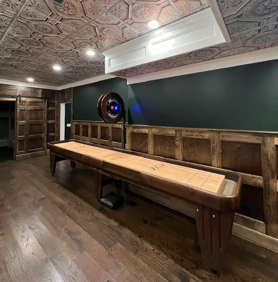 shuffleboard table with a scoreboard in a room with wood wainscoting and a green wall and a fancy retro ceiling