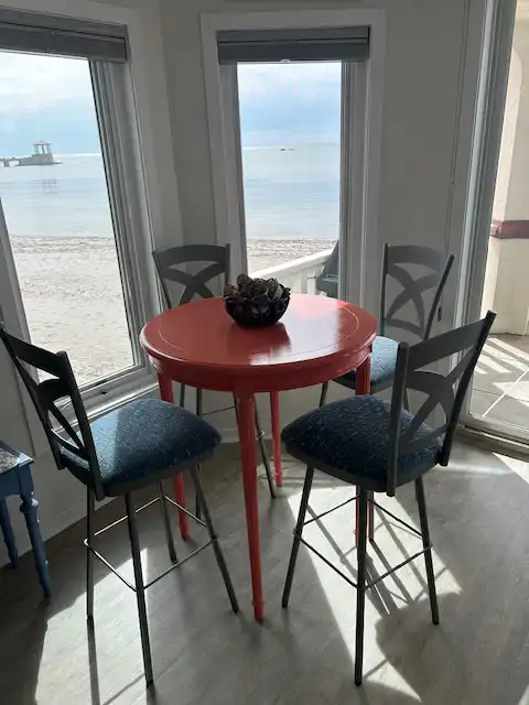 A well-set dining area with a table and bar stool chairs positioned elegantly before a large window on the beach