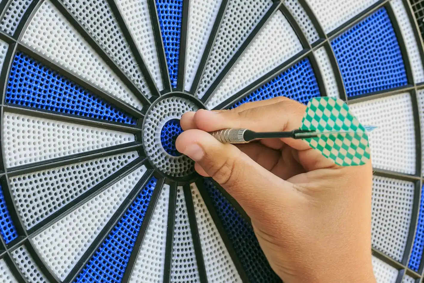 Bullseye on a wall with blue and grey electronic dartboard and green darts