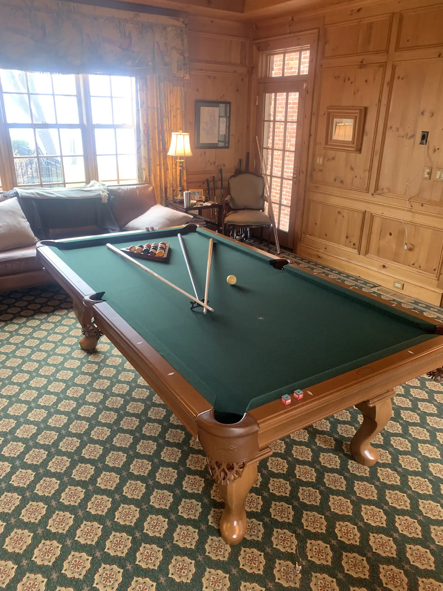 Green pool table with green pattern rug and wood panel interior of the room