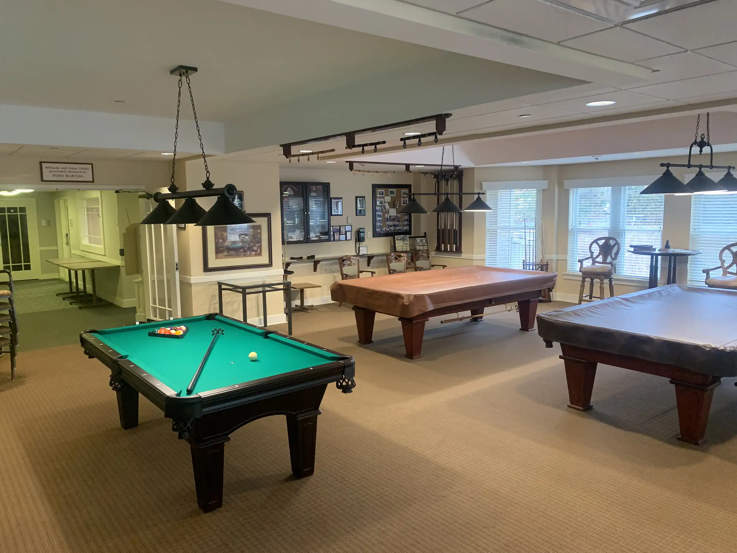 pool room (green) with three pool tables, cue racks, spectator seating, and billiard lighting at Masonicare in Wallingford, CT