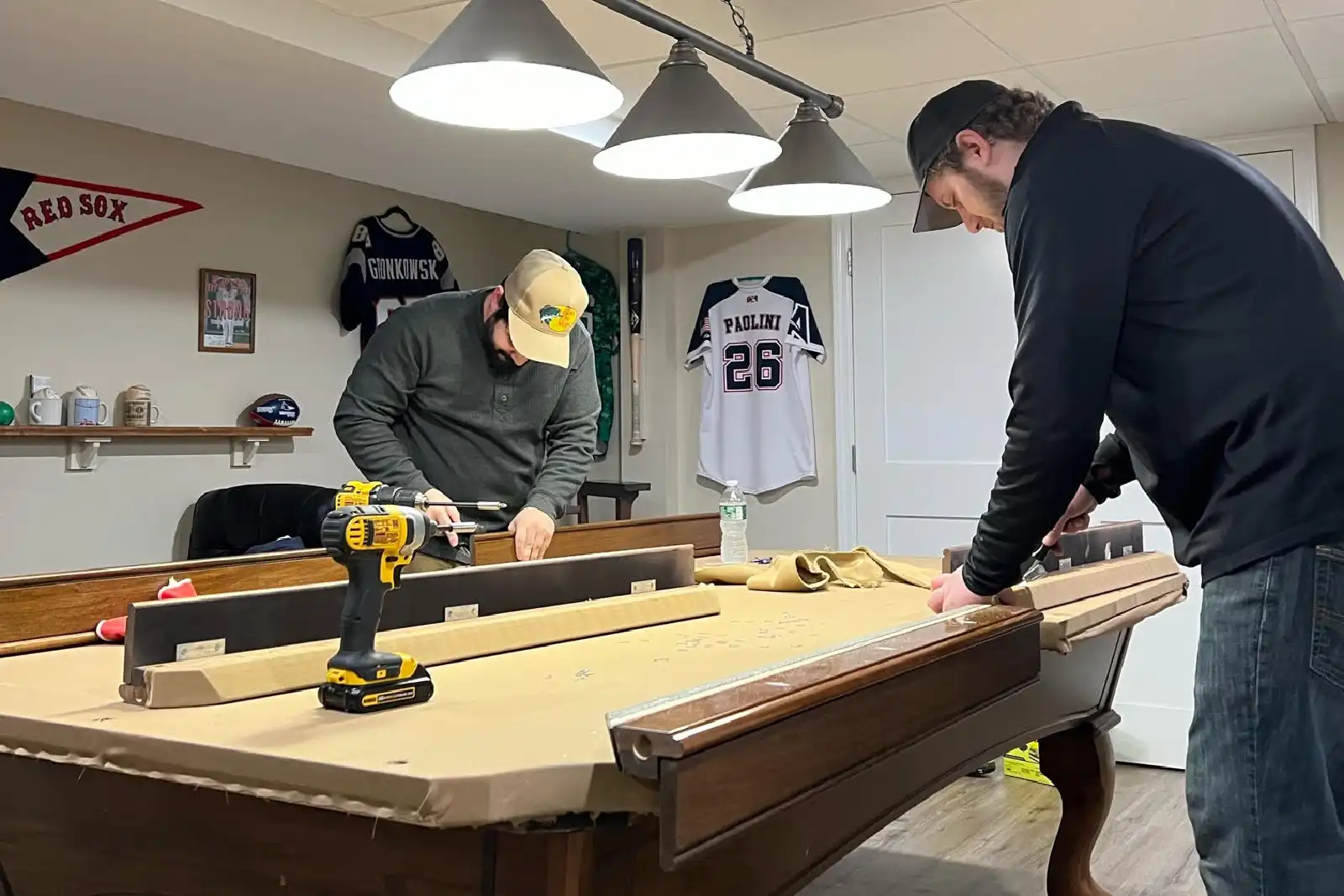 Two men re-felting a pool table in a basement during an installation
