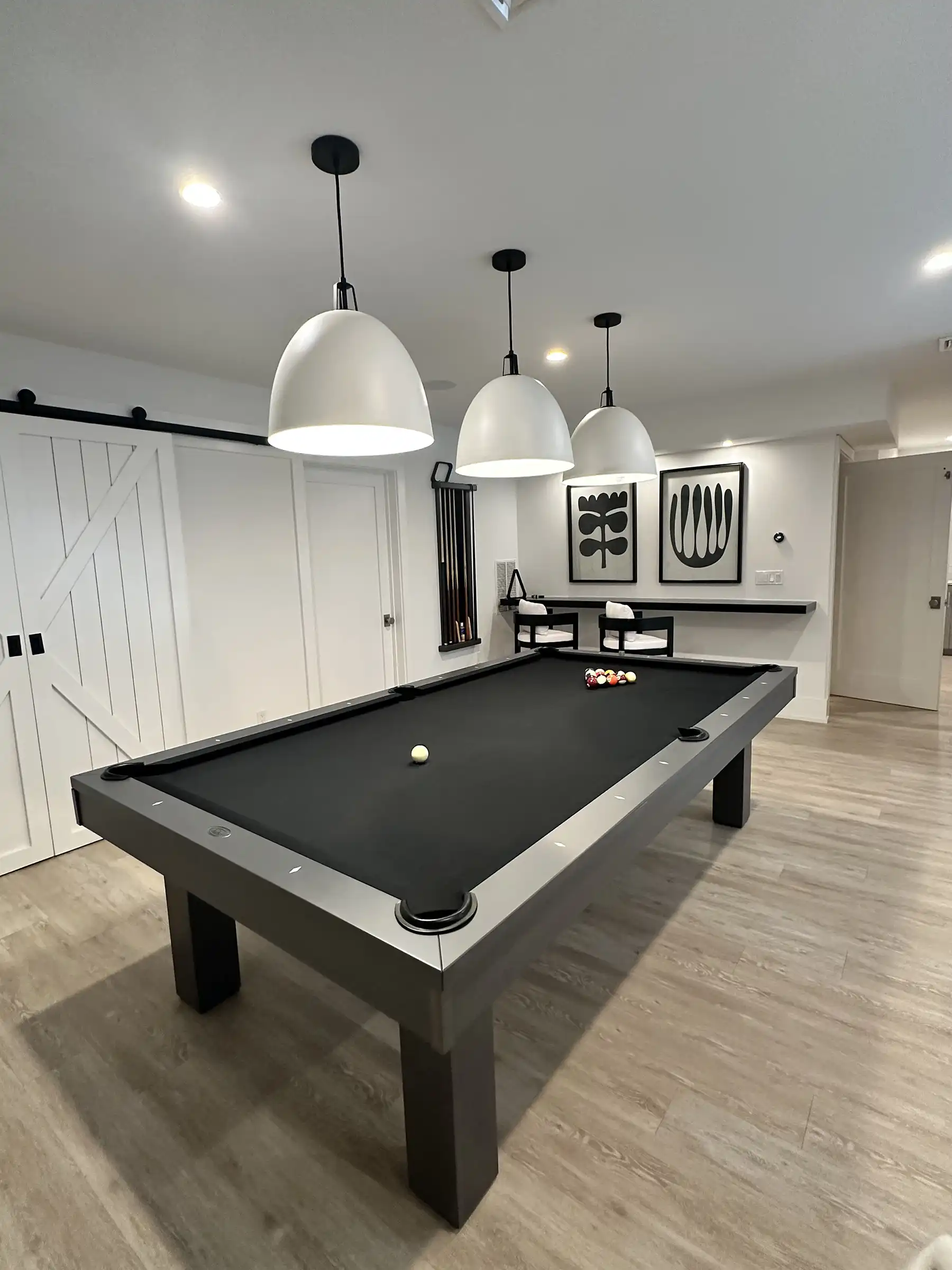 Modern black pool table with white lights and artwork in a sleek basement game room.