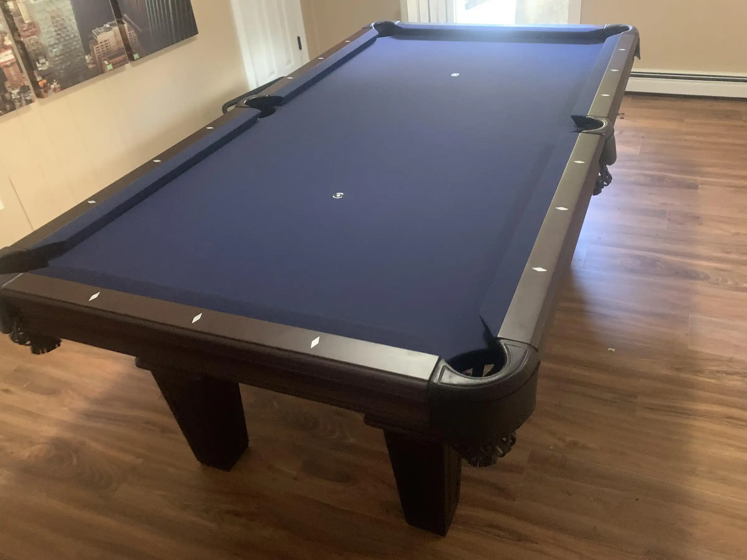 Olhausen Belmont pool table with a blue felt surface and wooden frame in a room with hardwood floors and cityscape wall art.