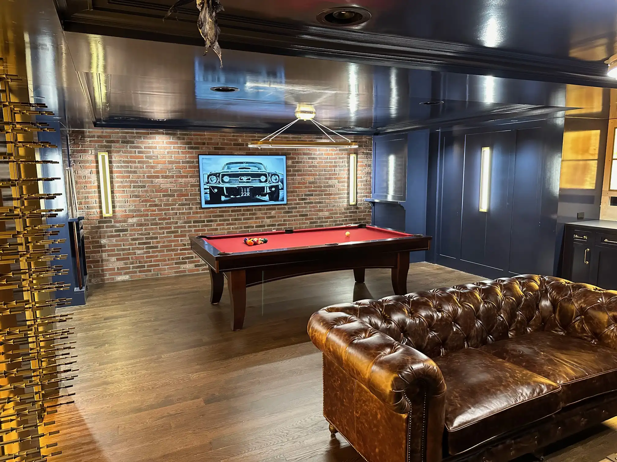 Brunswick Winfield Espresso pool table with red felt in a modern game room setting, featuring a leather sofa, brick accent wall, and unique lighting.