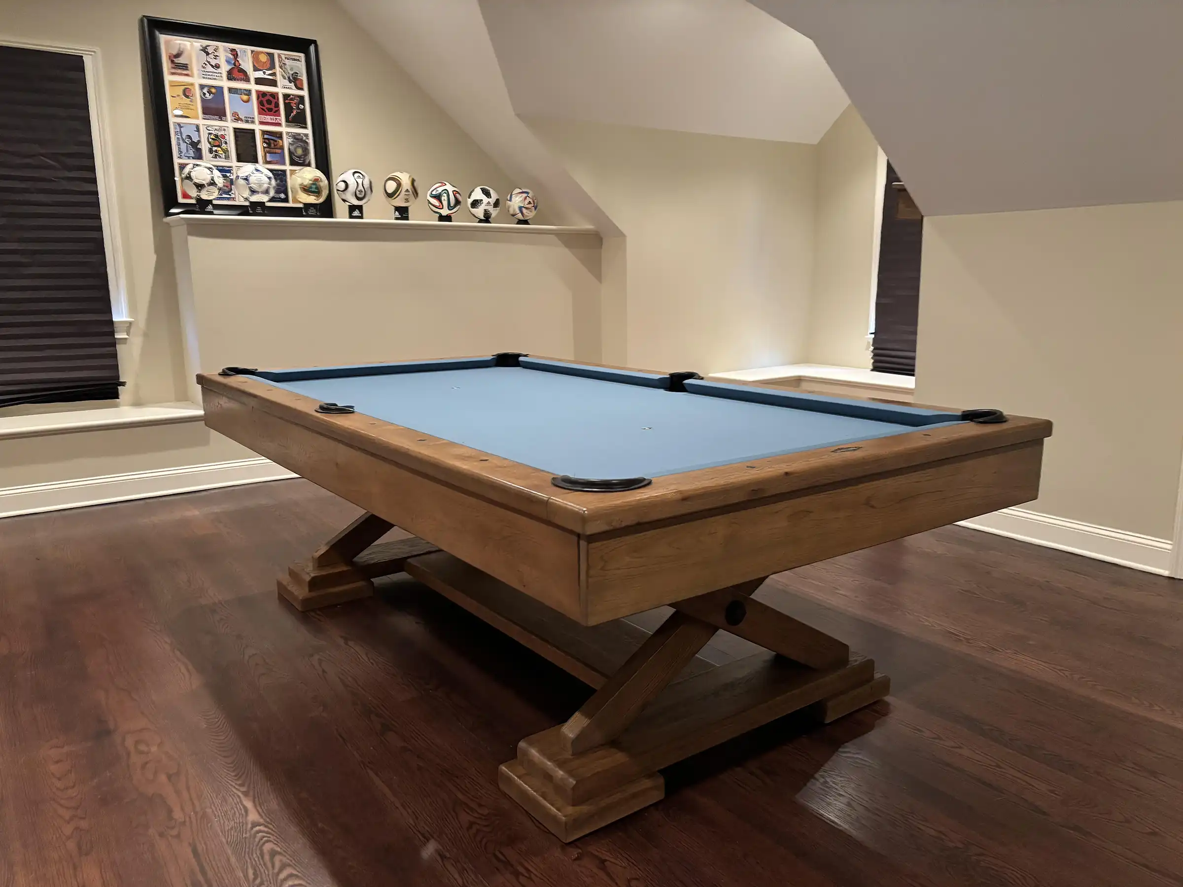 Classic Brunswick Brixton pool table with a light oak finish and blue felt, showcased on a dark hardwood floor in a well-lit game room.