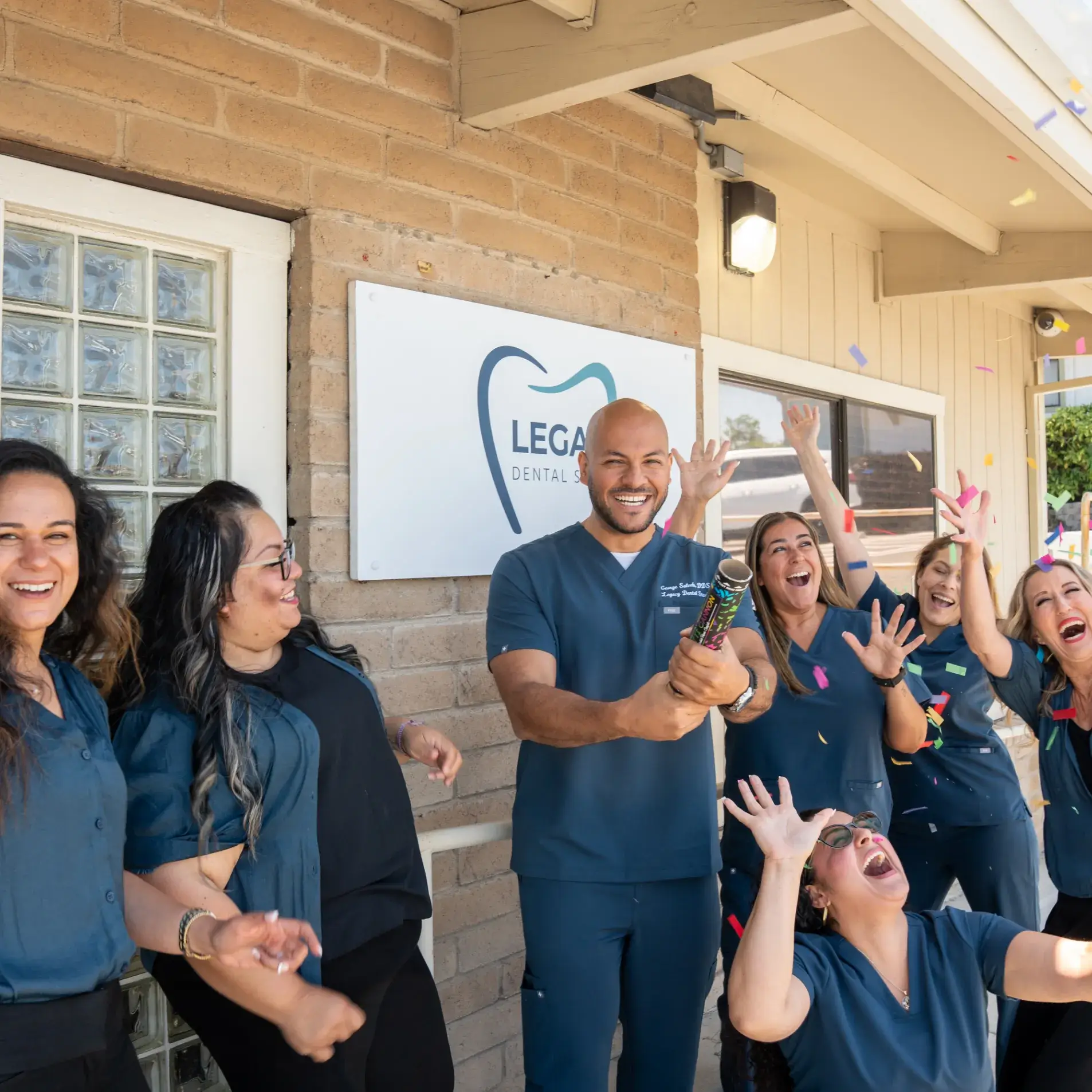 A group of people in dental uniforms celebrating outside a dental office with a confetti popper.
