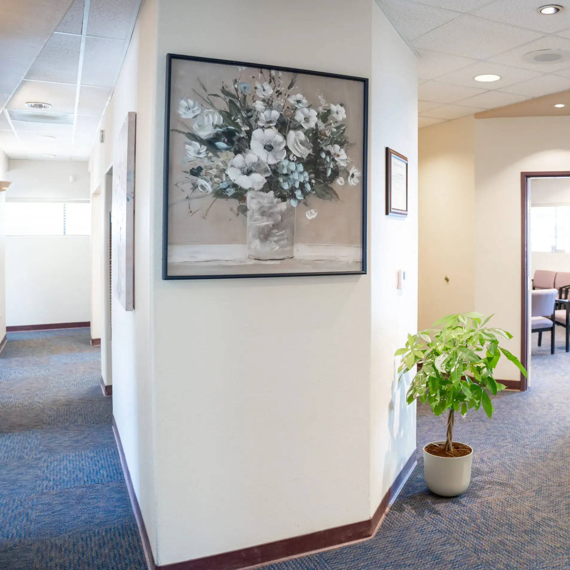 A hallway features a large painting of white flowers and a potted plant on the floor.