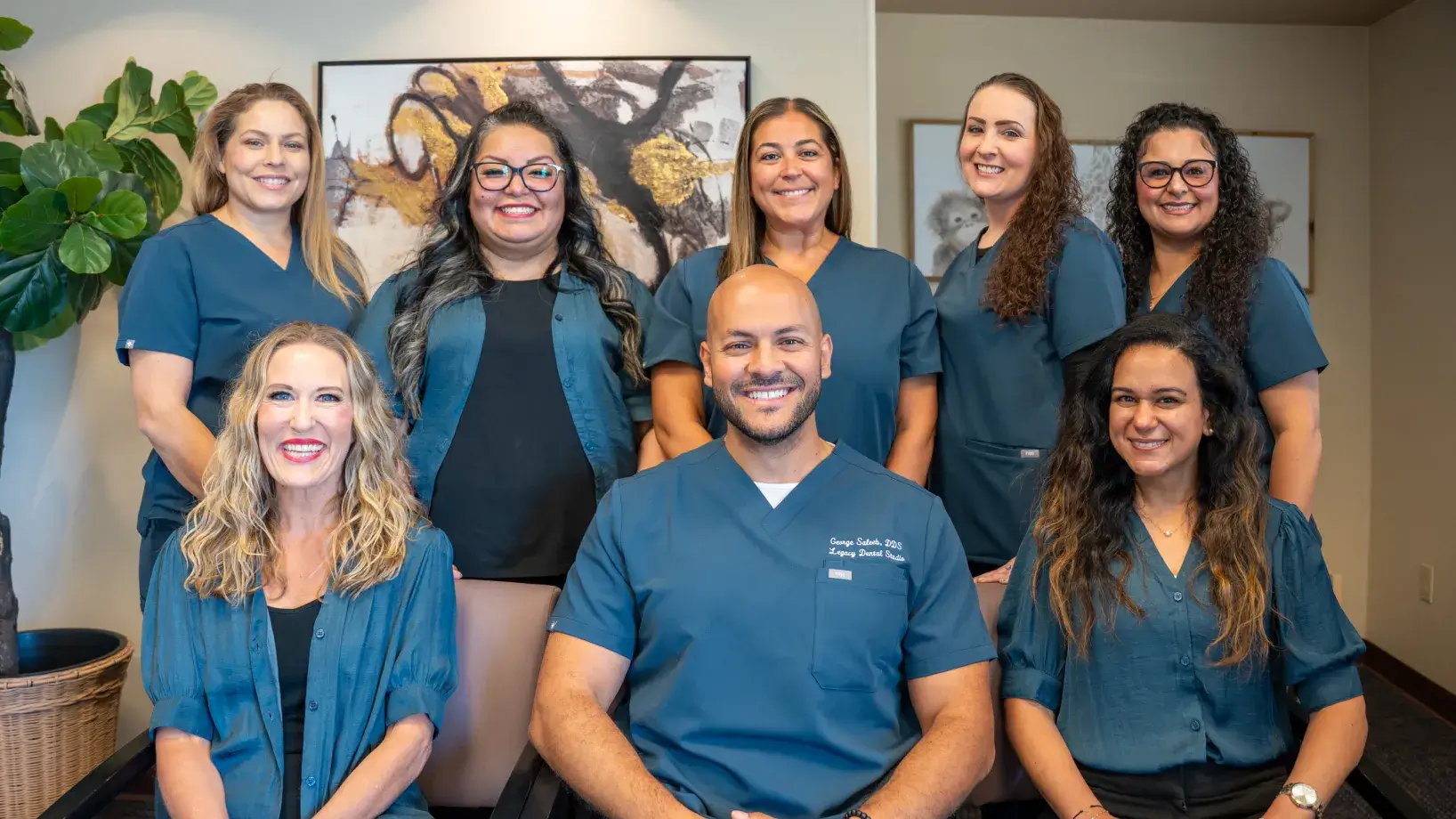 A group of eight smiling medical professionals in blue uniforms poses for a team photo indoors.