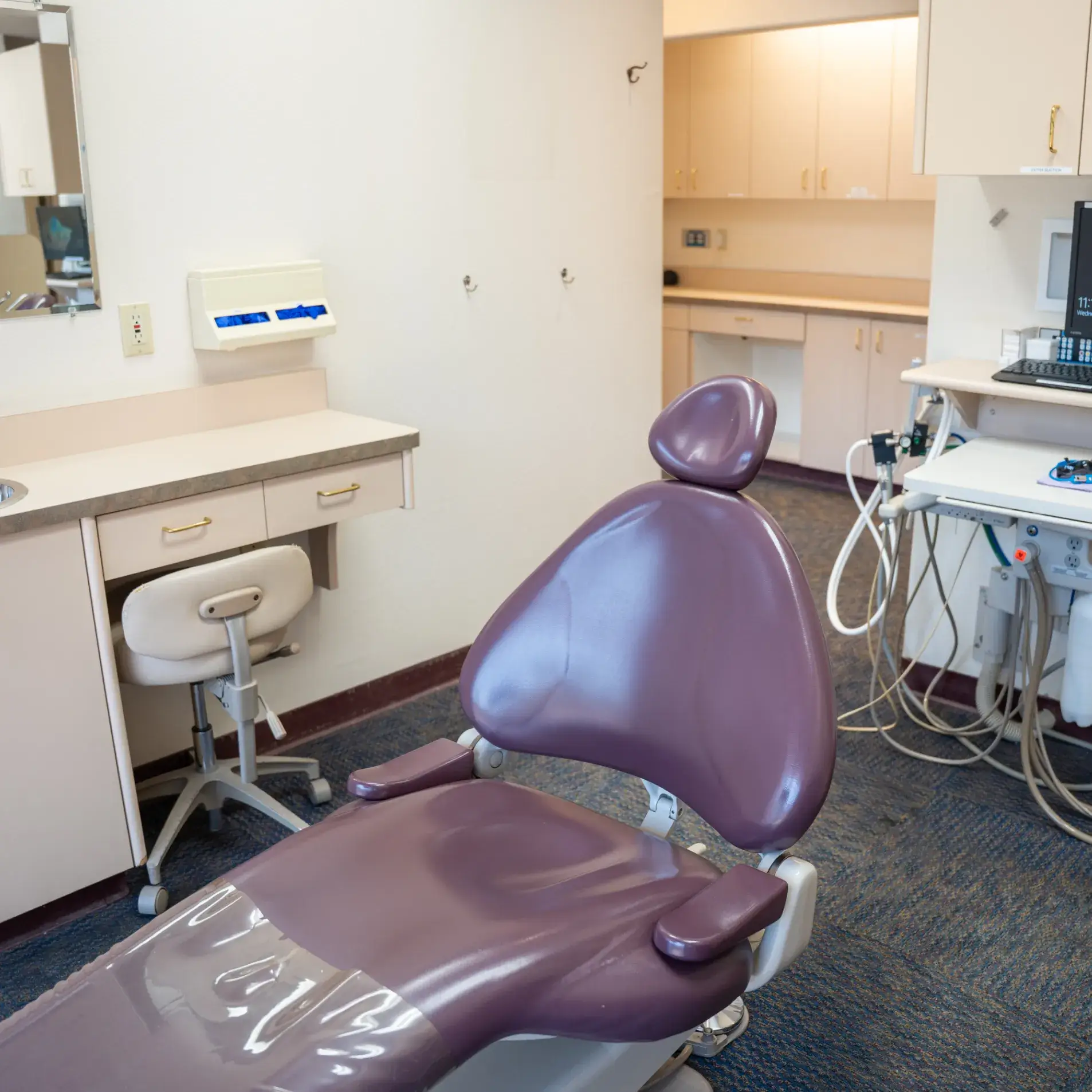 A dentist's chair in an empty room, with dental equipment and a small desk nearby.