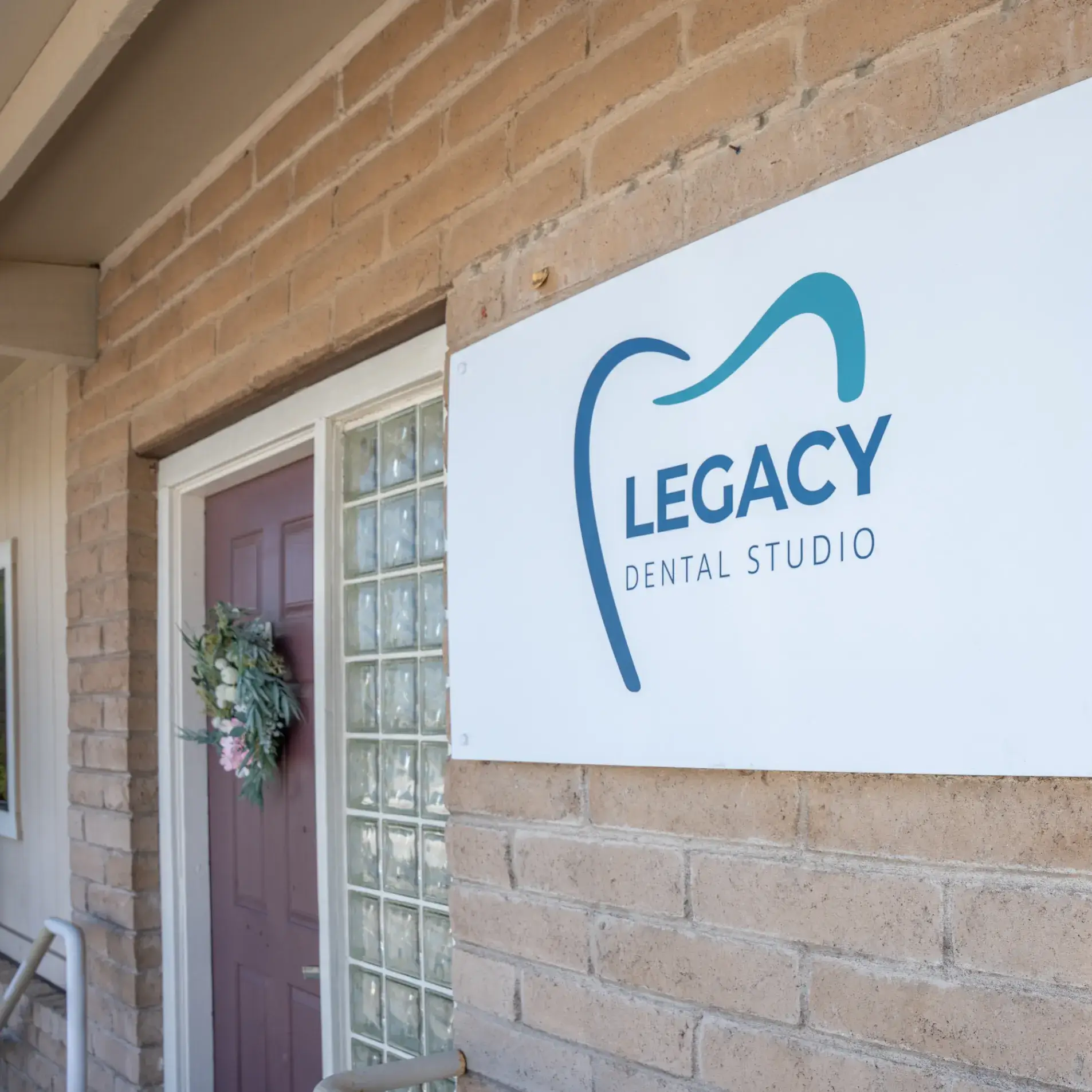 Sign reading "Legacy Dental Studio" on a brick wall near a door with a wreath.