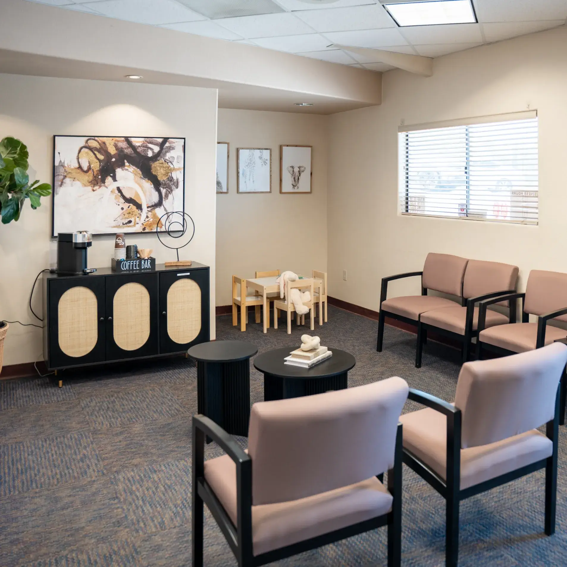 Small waiting room with pink chairs, a coffee bar, and children's play area with a table.