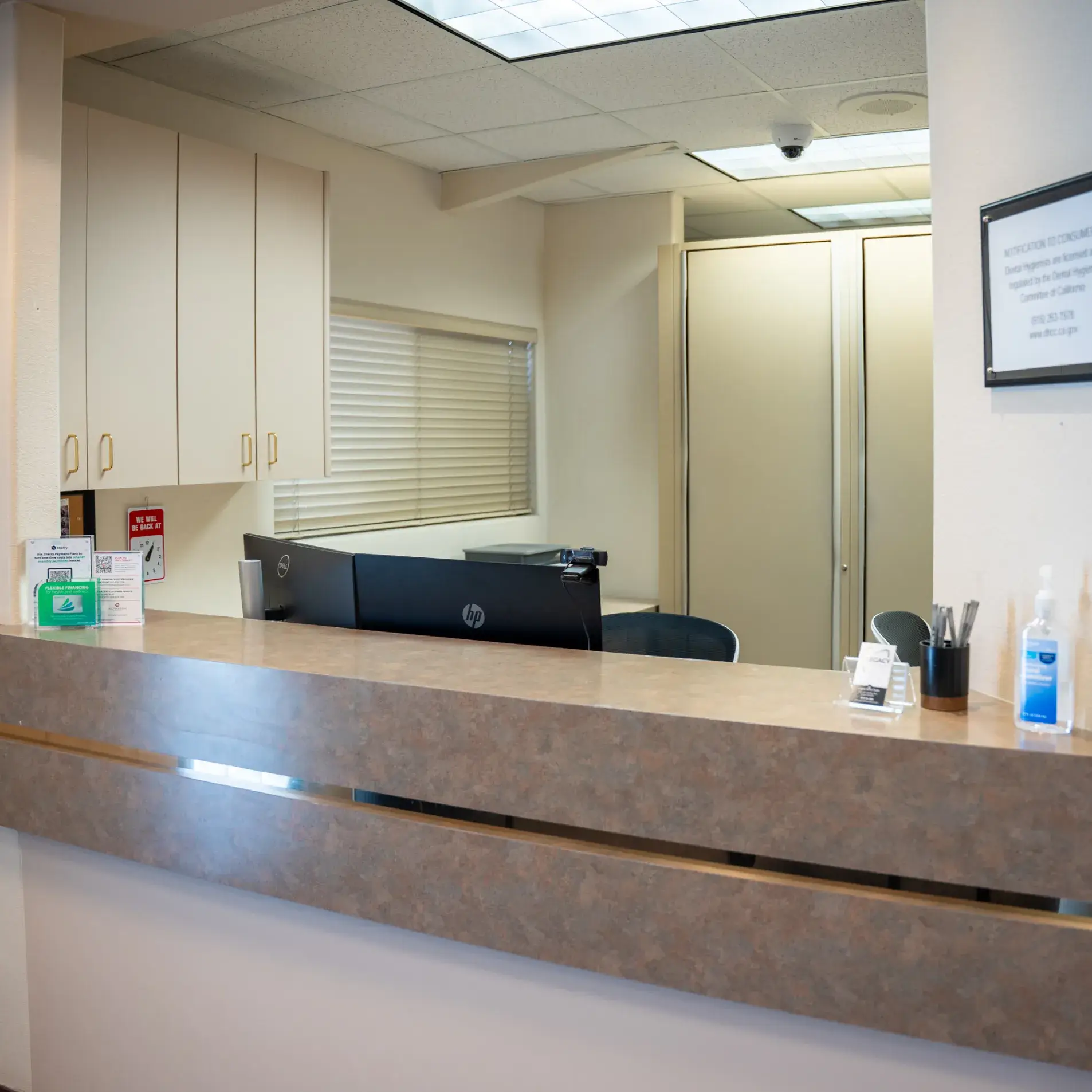 Medical reception desk with a computer, hand sanitizer, and sign-in sheet in an empty office.