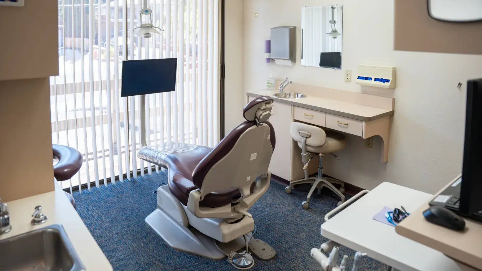 Dental chair in a clean, modern dentist's office with equipment and a computer screen nearby.