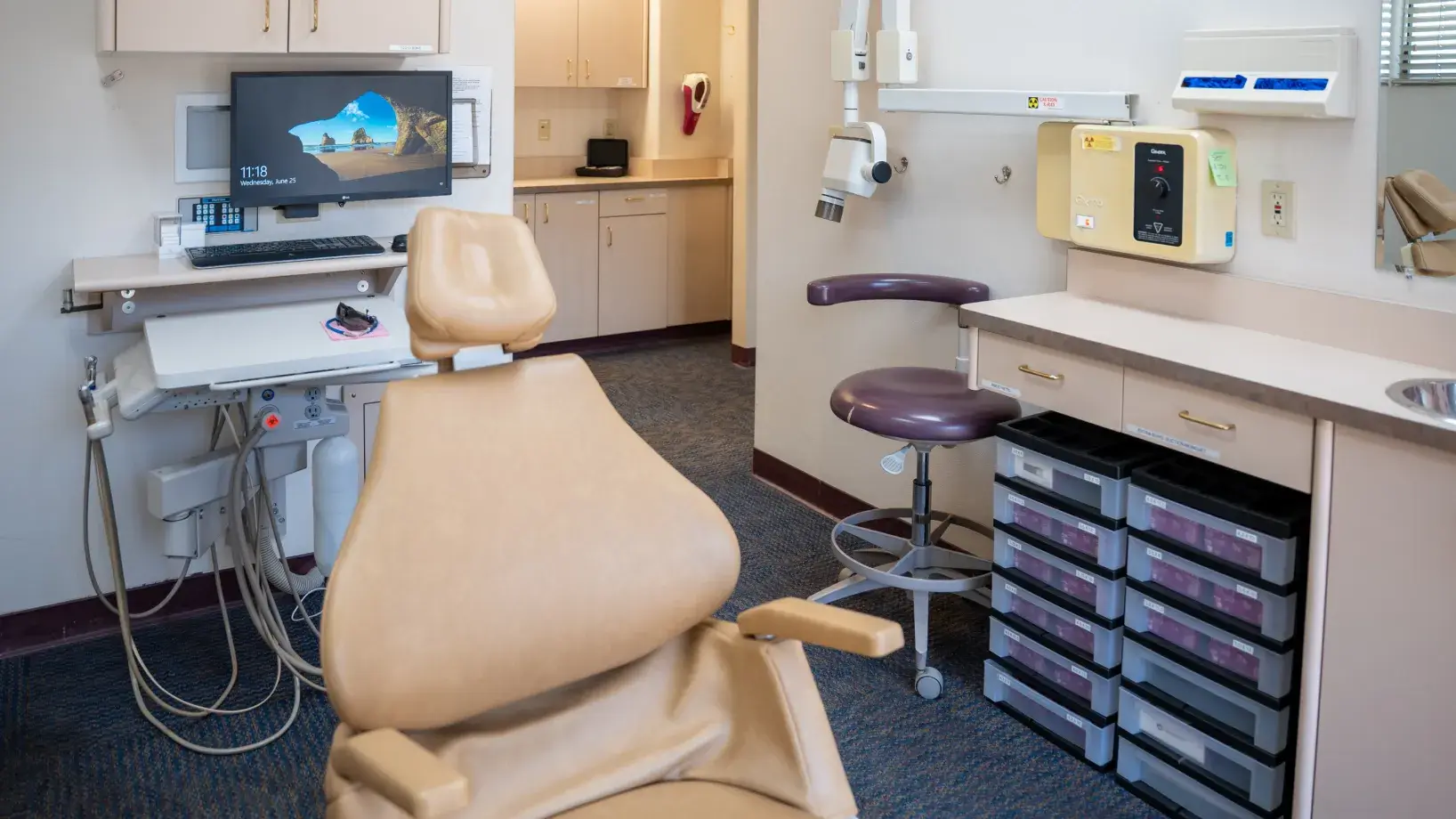 An empty dental office with a beige chair, computer monitor, and dental equipment.