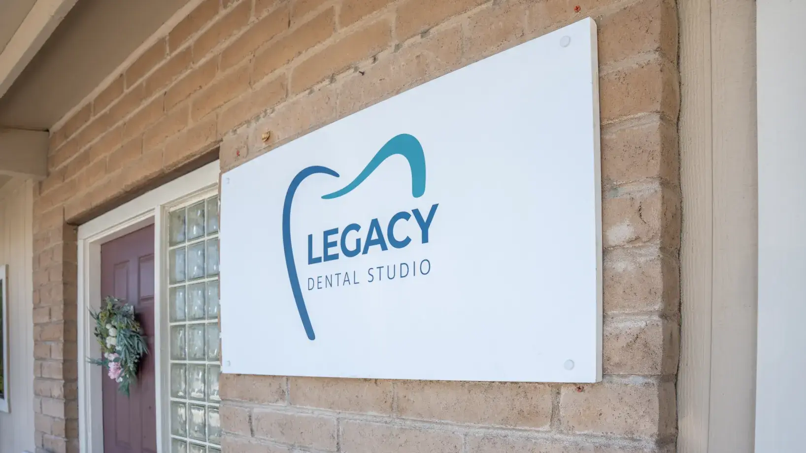 Sign on brick wall reads "Legacy Dental Studio" with a tooth logo.