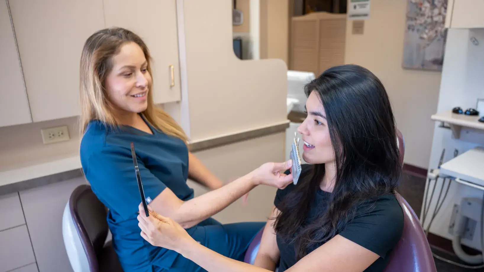 A dental professional shows a patient her teeth using a mirror and dental tool.