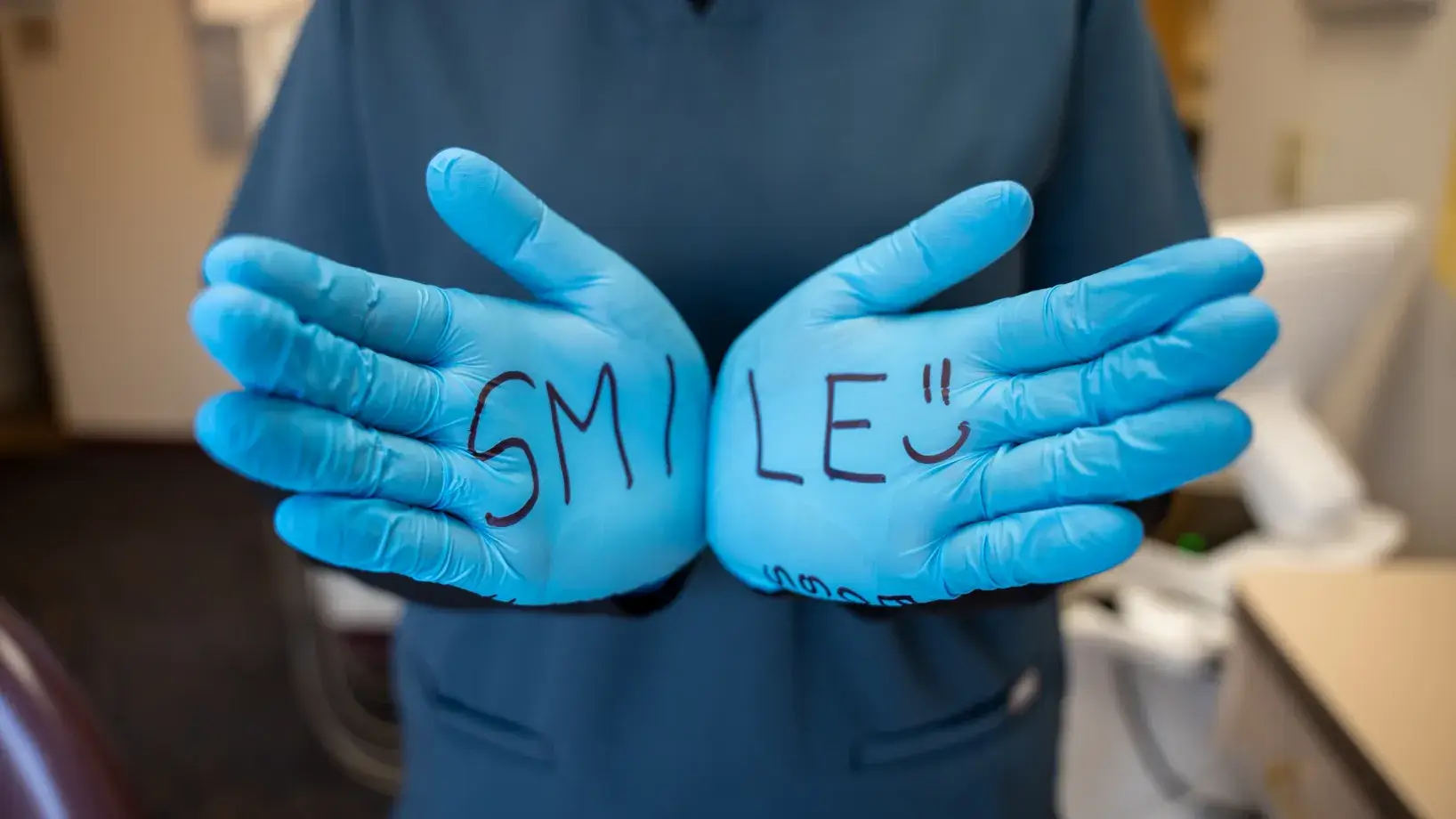 Person wearing blue gloves with "SMILE" written on them, standing indoors.