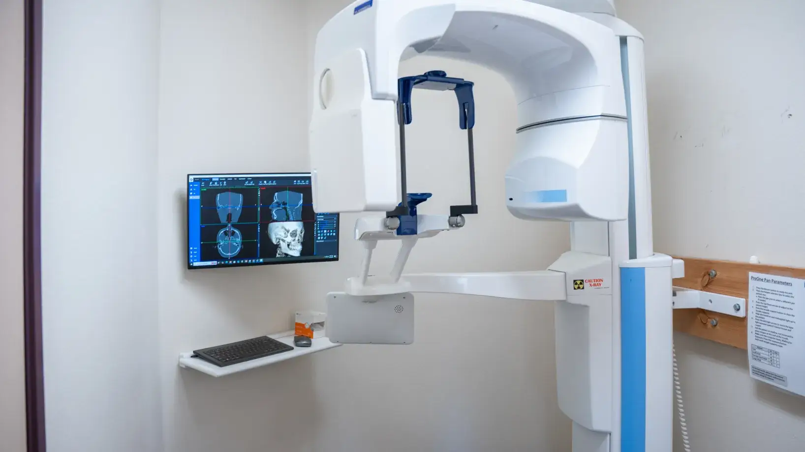 Dental imaging machine with a computer screen displaying detailed scans in a small examination room.