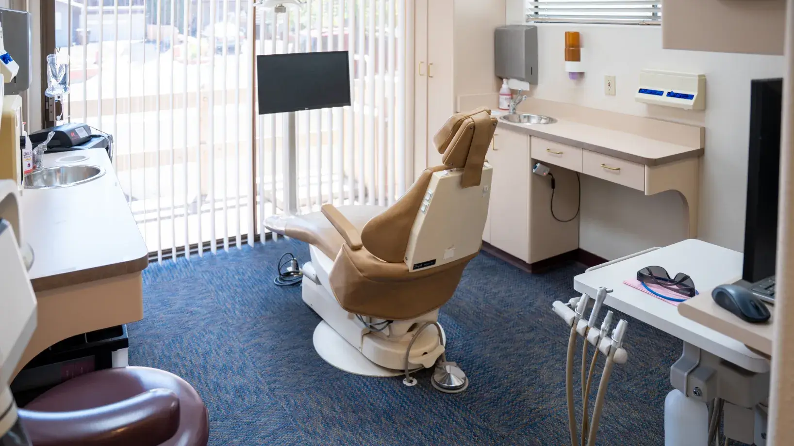 Dental office with an empty brown dental chair and equipment in a well-lit room.